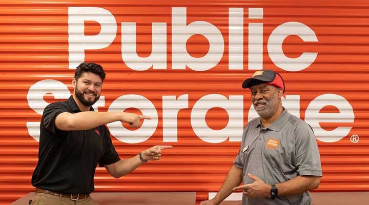 public storage employees smile while standing in front of orange door logo